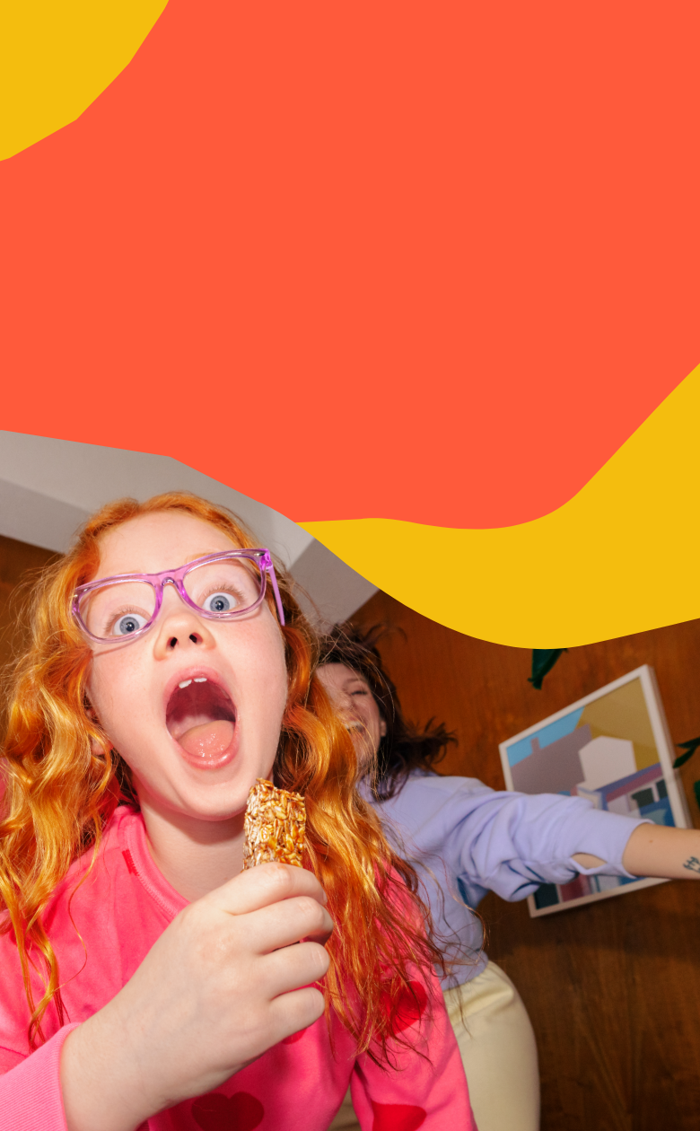 Child with red hair and pink glasses holding a MadeGood granola bar against a colorful background abstract background Child with red hair and pink glasses holding a MadeGood granola bar against a colorful background abstract background