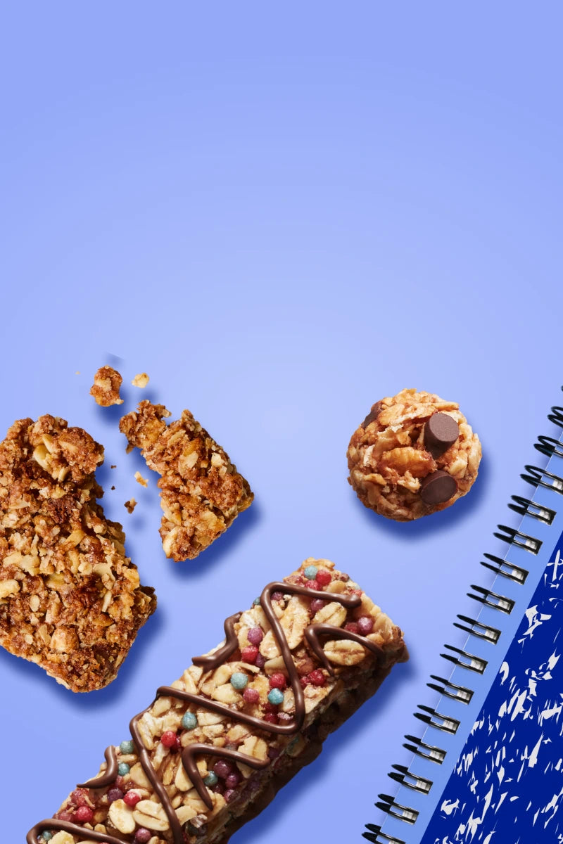 A MadeGood bar piece with oats and dark chocolate in it on a blue background