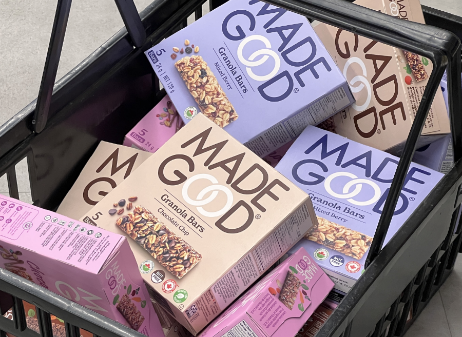 A shopping basket filled with various boxes of Made Good granola bars in oatmeal and mixed berry flavors, featuring earthy-toned packaging.