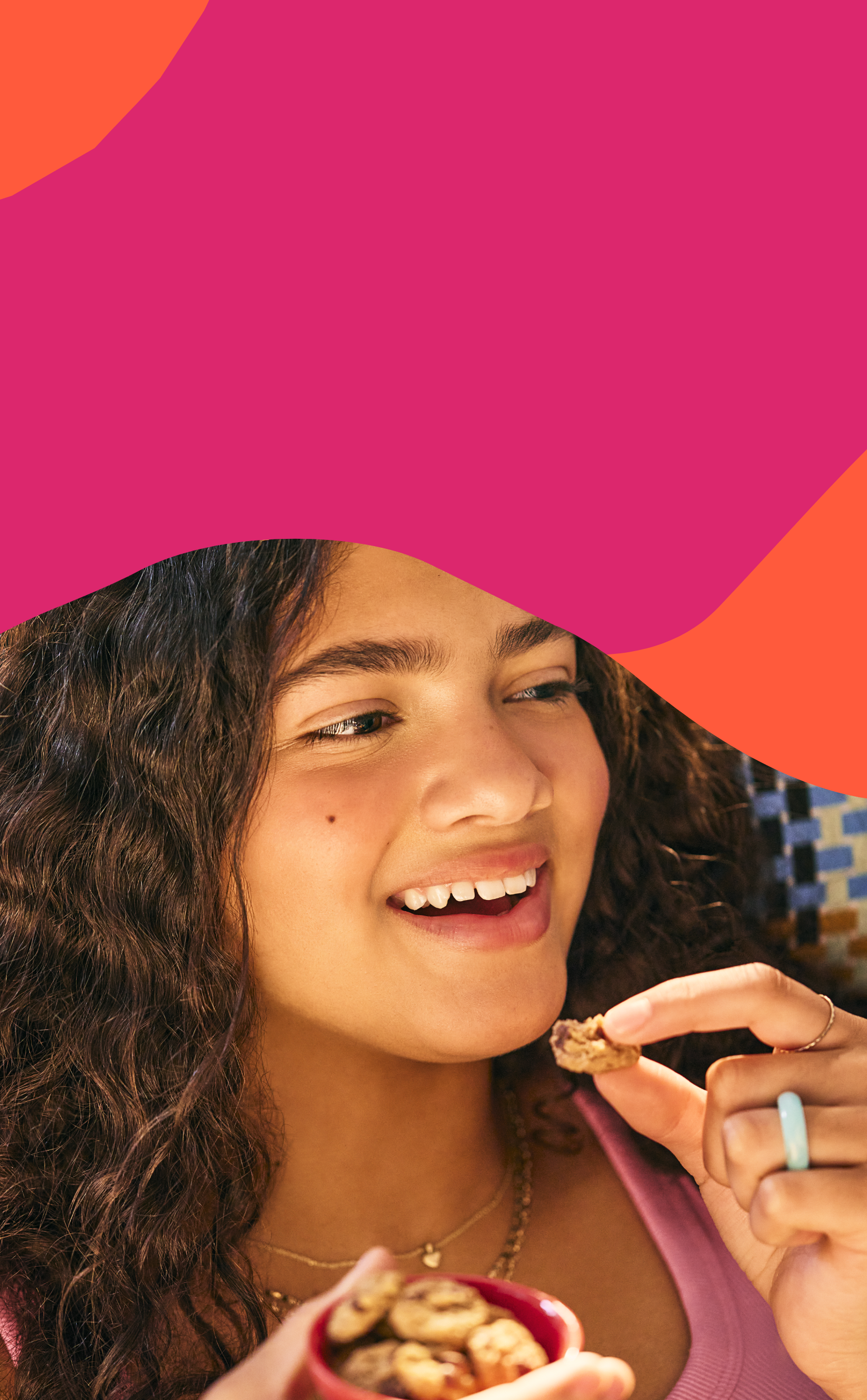 Girl eating MadeGood soft baked cookies on a pink and orange abstract background.