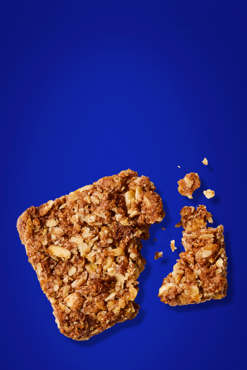 A MadeGood bar piece with oats and dark chocolate in it on a blue background